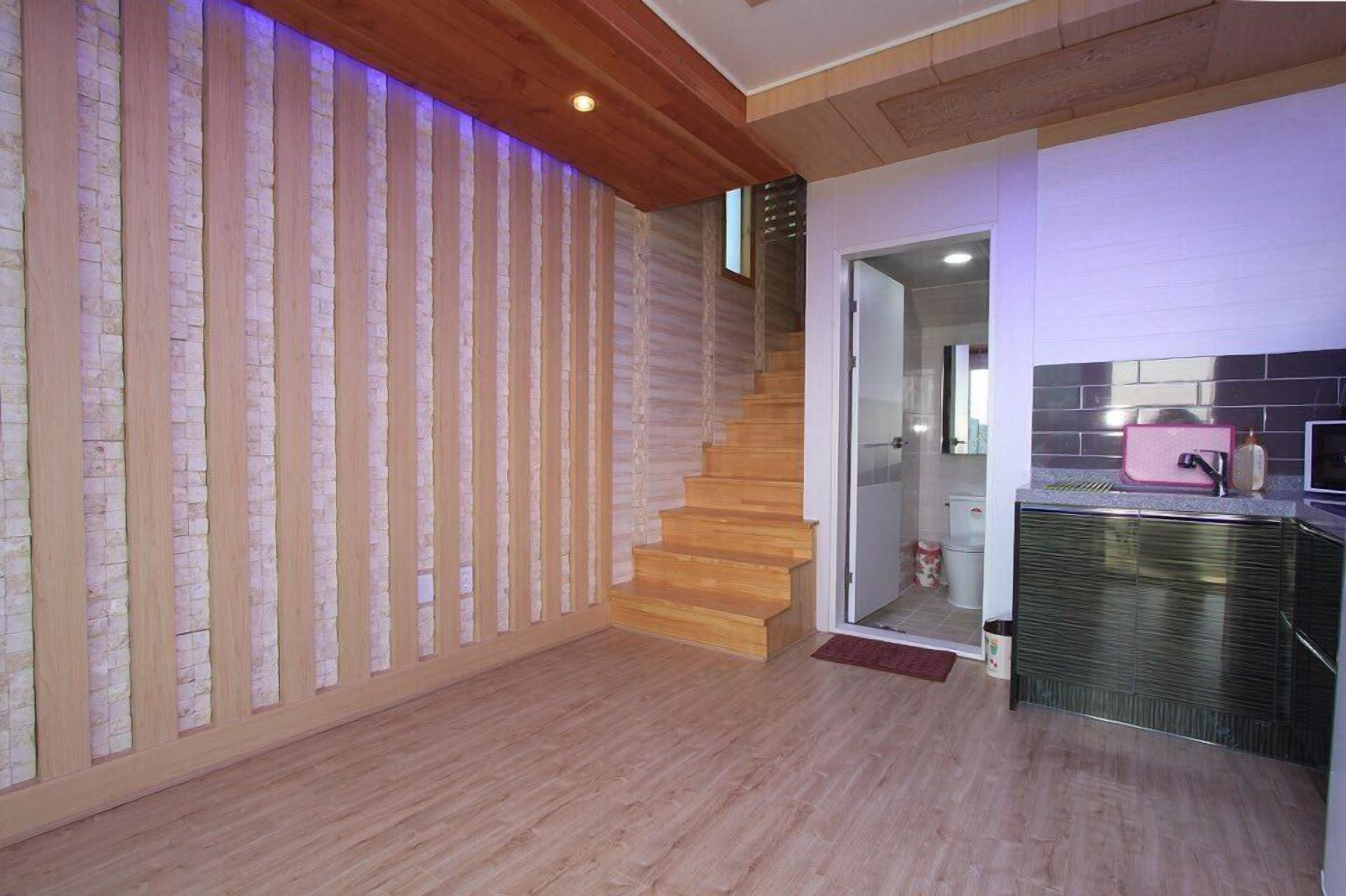 A modern kitchen with a wooden staircase, a kitchen island, and a view of the living area.