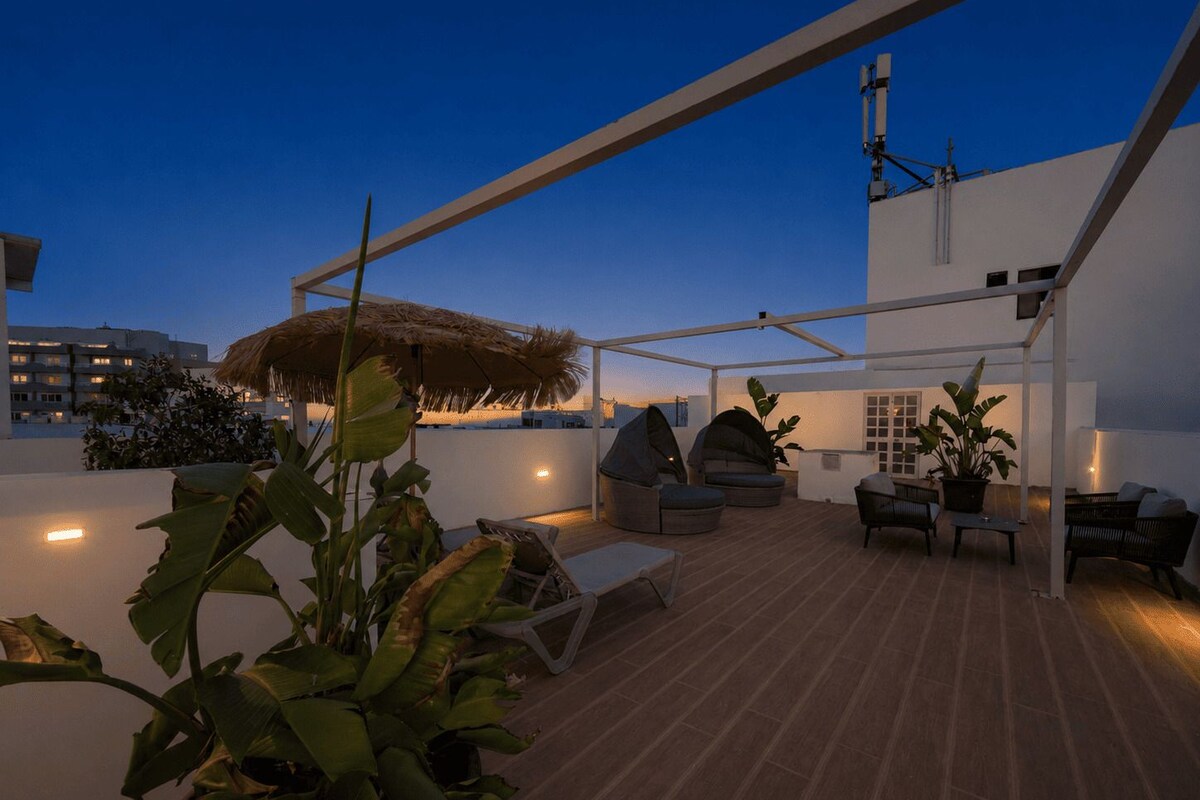 Un patio al aire libre con mobiliario, techo de paja y plantas en macetas.