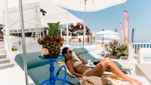 A lounge area with a hookah, a pineapple with strawberries, and a person relaxing on a sunbed.