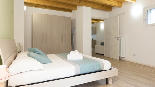 A modern bedroom with a wooden ceiling, a bed with white bedding, a light blue pillow, and a neatly made bed with towels. - Residenze Lariane apartment Edera (Colico Piano)