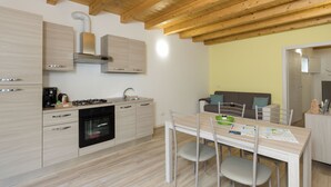 A modern kitchen with wooden cabinets, a gas stove, and a built-in oven. There is a dining area with a table and chairs, and a sofa in the background. - Residenze Lariane apartment Edera (Colico Piano)