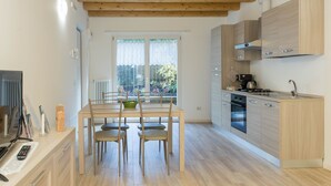 A modern kitchen with wooden cabinets, a dining table with chairs, and a large window with a view of greenery. - Residenze Lariane apartment Edera (Colico Piano)