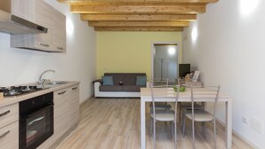 A compact kitchen with a wooden ceiling, a dining area with a table and chairs, and a sofa in the background. - Residenze Lariane apartment Edera (Colico Piano)