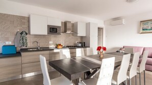 Une cuisine moderne avec des meubles blancs, un îlot central et un coin repas comprenant une table et des chaises.
