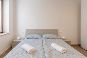 Un lit double avec une couvre-lit à motifs, deux oreillers et deux serviettes enroulées sur une table de chevet.