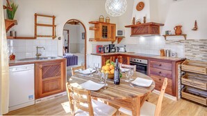 A kitchen with wooden cabinets, a dining table set with plates and glasses, and a hanging light fixture. - Finca “Ses Begudes” with Garden, Terrace, Pool, Air Conditioning & Wi-Fi (Fornalutx)