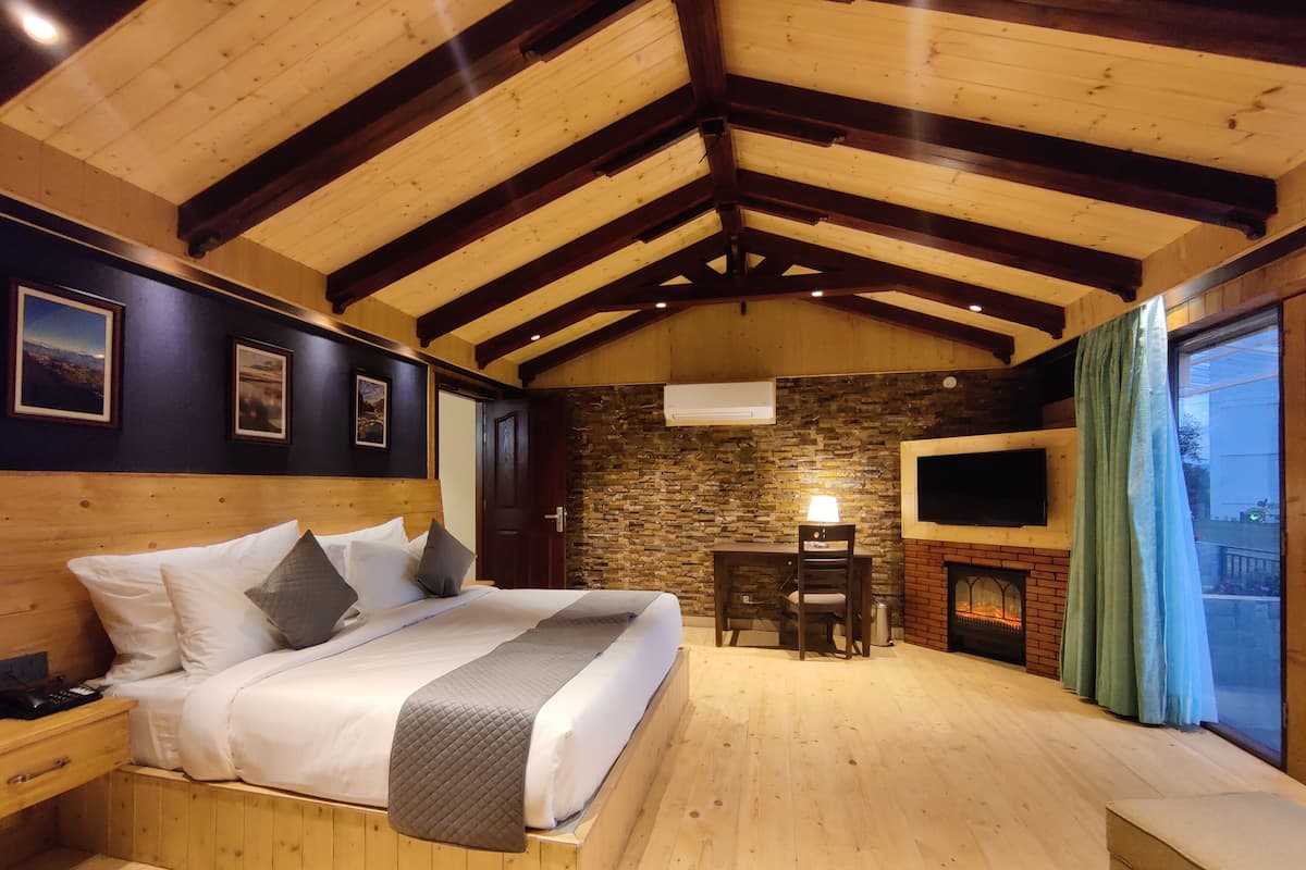A cozy bedroom with a wooden ceiling, a stone wall, a fireplace, a TV, and a bed with pillows.