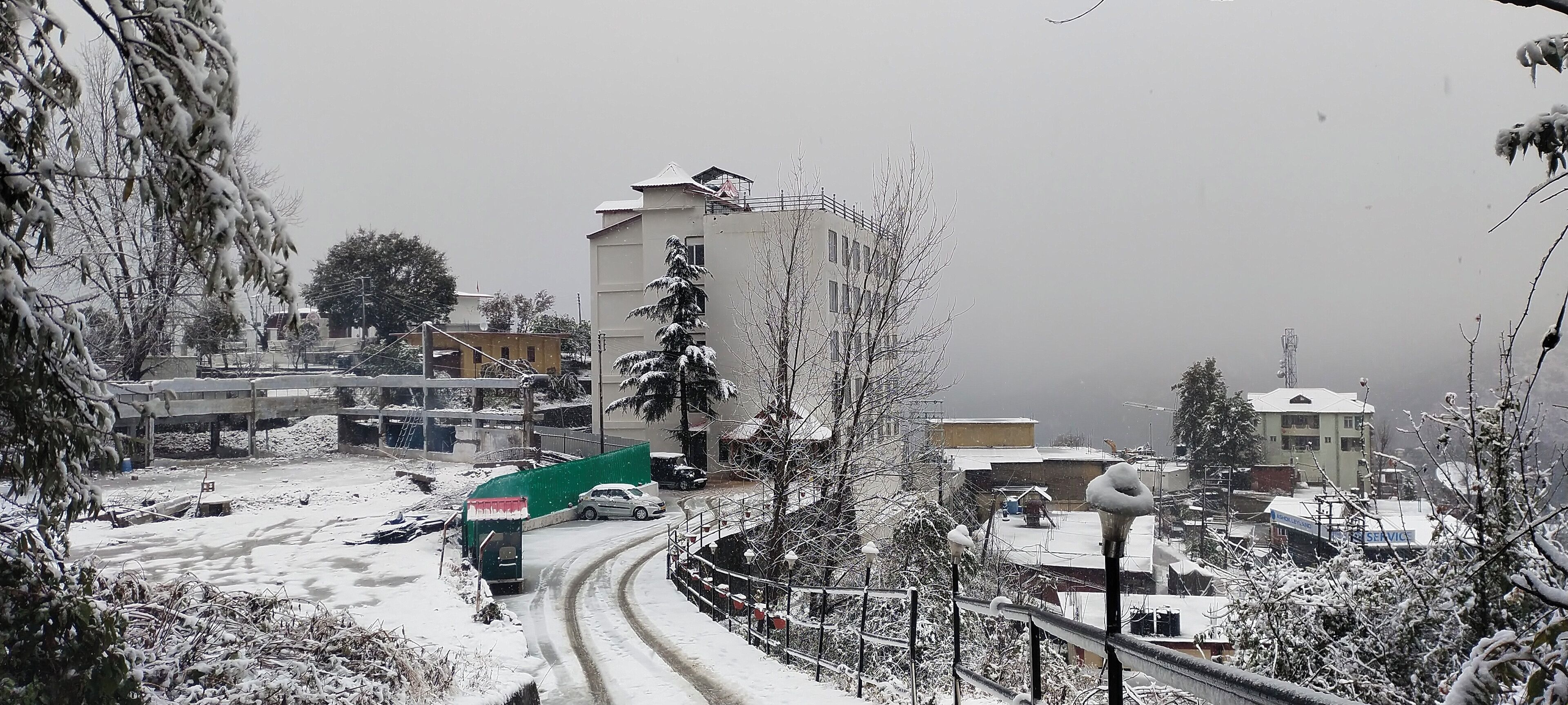 A snowy residential area with buildings, a curved road, and a green sign.