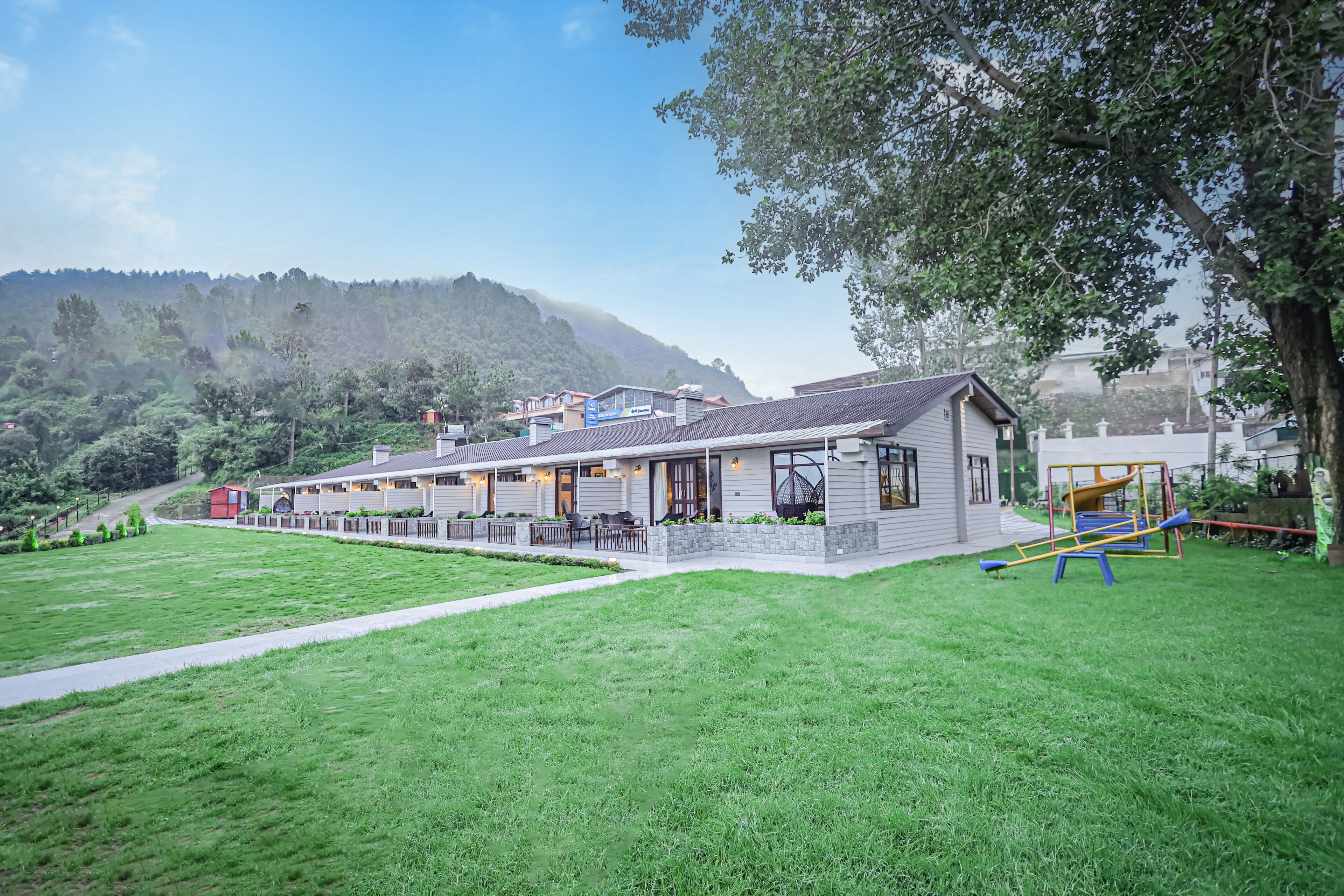 A building with a patio area, a playground, and a view of a hilly landscape.