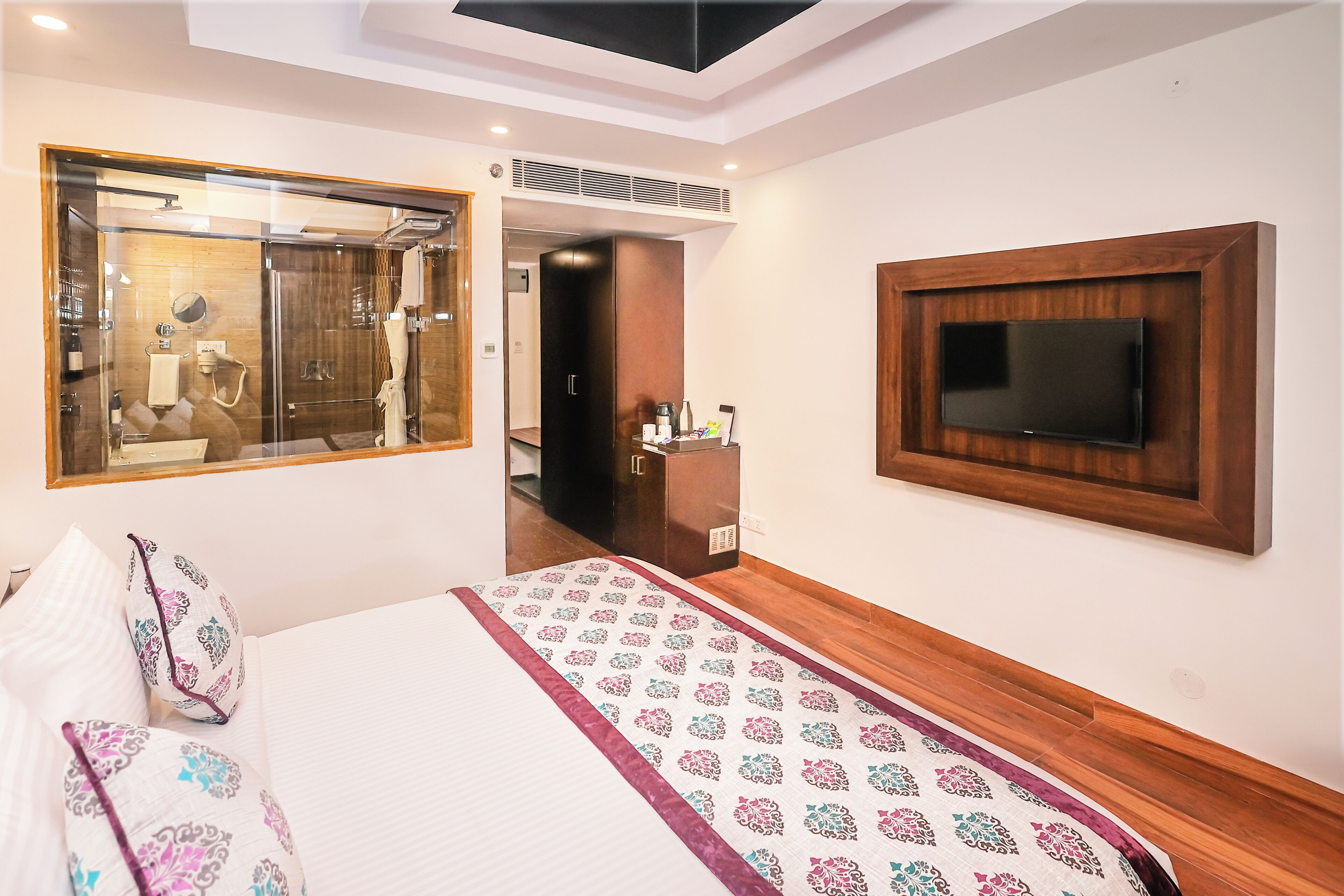 A hotel room with a bed, a TV mounted on the wall, a mirror, and a shower area.