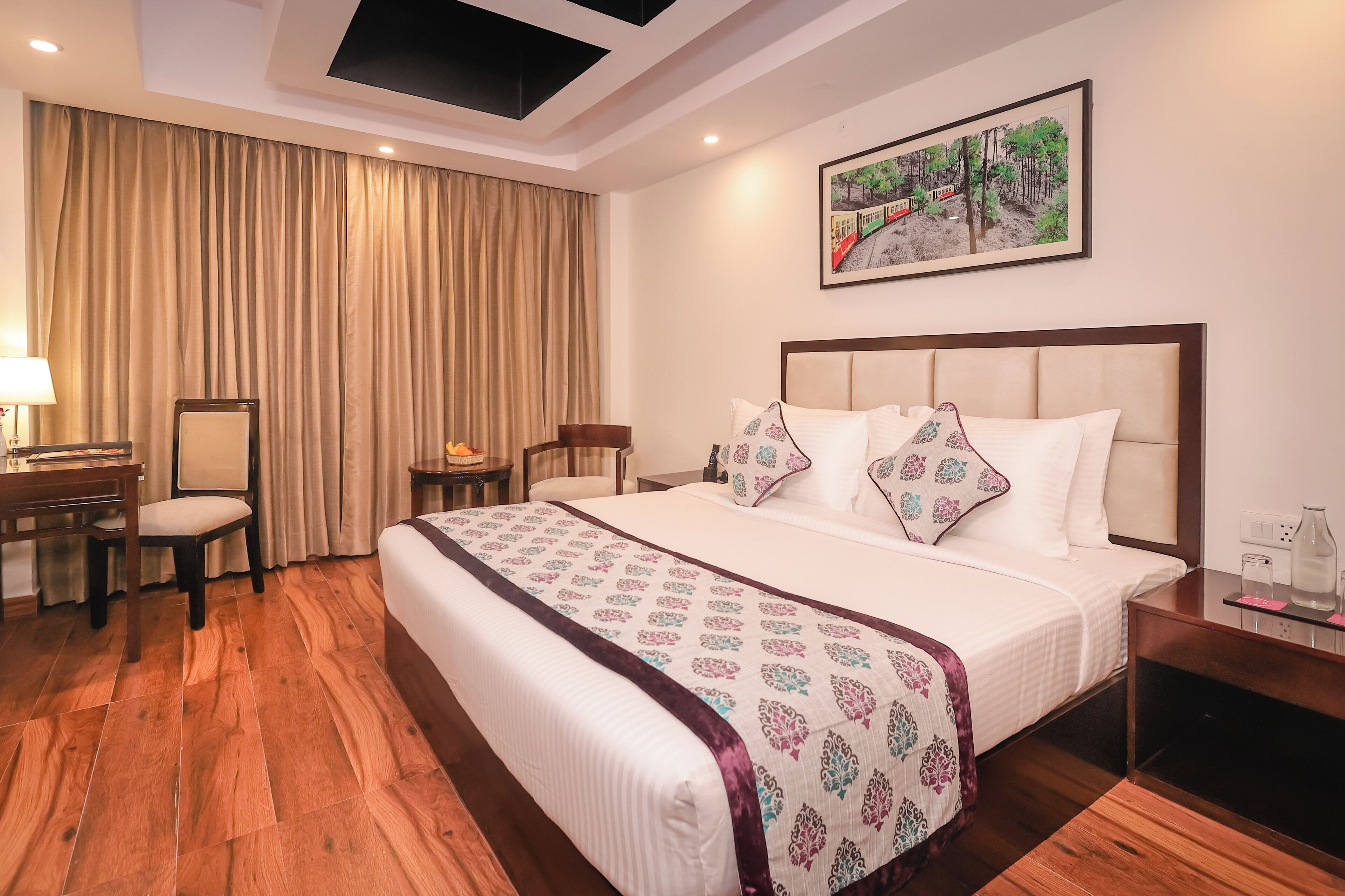 A hotel room with a large bed, a desk, a chair, a small table, and a painting on the wall.