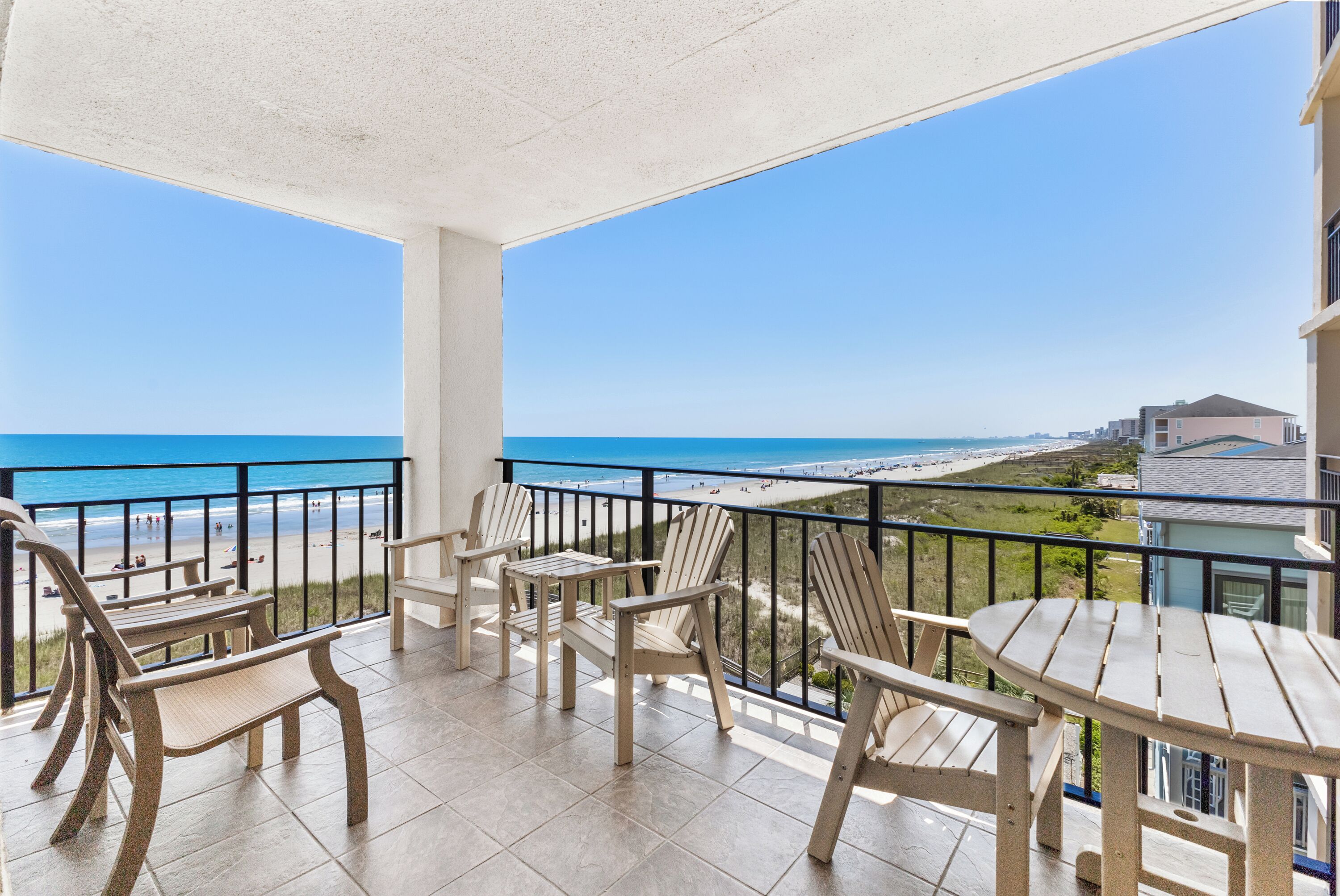 A balcony with chairs and a table overlooking a beach.