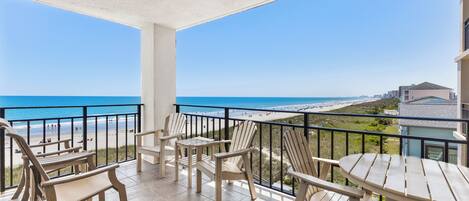 A balcony with chairs and a table overlooking a beach.