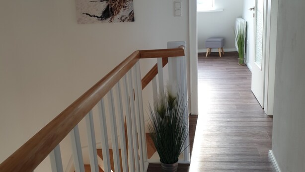 Een trap met houten leuningen die uitkomt op een plateau met een plant in pot.