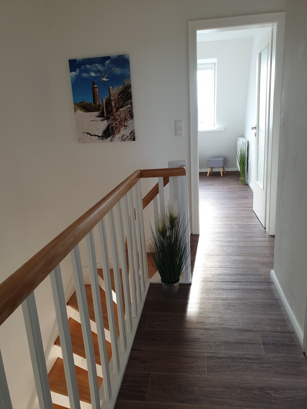 Eine Treppe mit hölzernen Geländern führt zu einer Zwischenebene mit einem Blumentopf.