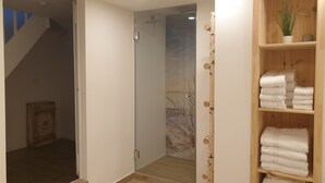 Een moderne badkamer met een glazen douchecabine, een houten plankje met opgevouwen handdoeken en een zichtbare trap die naar een andere kamer leidt.