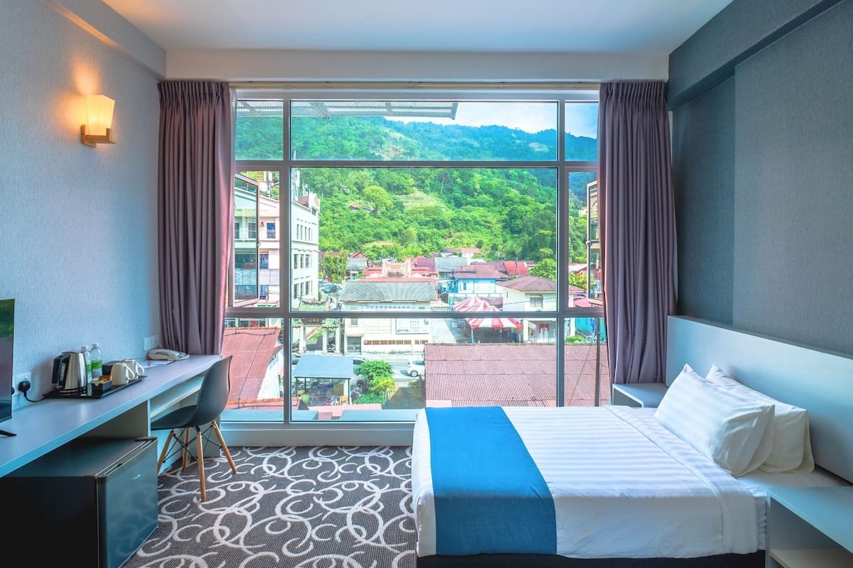 A hotel room with a large window, a bed, a desk, and a chair.