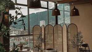 Ein Essbereich mit großem Fenster, Korbstühlen, einem runden Tisch und hängenden Lampen.