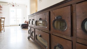 Eine Holzkommode mit mehreren Schubladen und Glastüren, ein Holzstuhl und im Hintergrund ein Essbereich mit Tisch und Stühlen.
