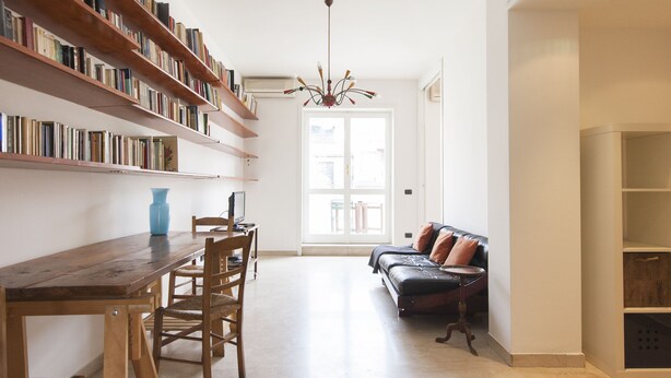 Ein geräumiger Raum mit einem Holzespeisetisch, Stühlen, einer Couch und einem Bücherregal voller Bücher.