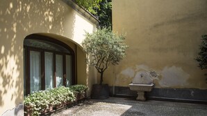 Un patio con un árbol en maceta, un banco de piedra y una ventana que da al jardín.