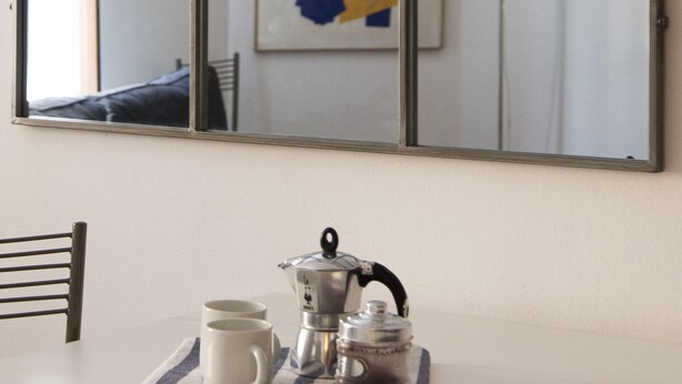 Habitación con un espejo grande que refleja una cama y una pared con arte abstracto. Hay una mesa con un hervidor y tazas.