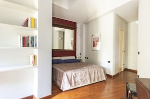 A bedroom with a bed, a bookshelf, a mirror, and a door.