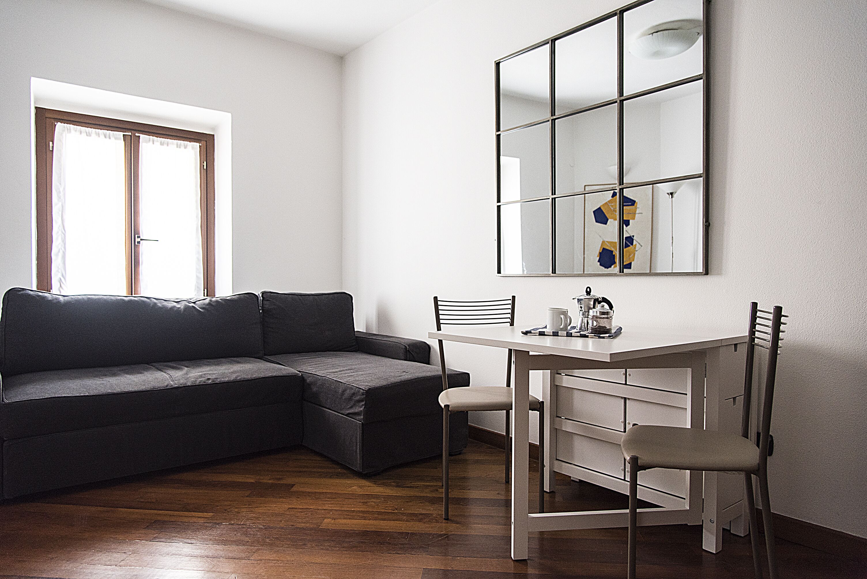 A modern living room with a sectional sofa, a dining table with two chairs, and a large mirror on the wall.