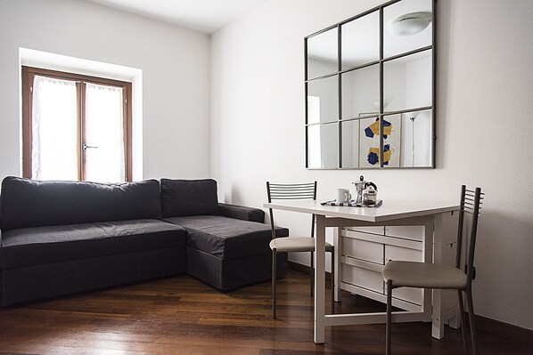 A modern living room with a sectional sofa, a dining table with two chairs, and a large mirror on the wall.