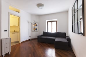 A spacious living room with hardwood flooring, a dark grey sectional sofa, a small side table, and a framed abstract artwork on the wall.