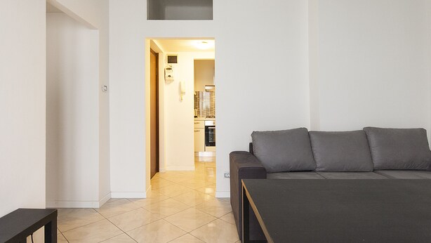 A modern living room with a sofa and a small table. A kitchen is visible in the background. - Studio Flat in a Quiet Place (Milan)
