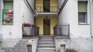 A building with a staircase leading to a second-floor balcony. There is a potted plant on the left balcony and a decorative figure on the right balcony. - Studio Flat in a Quiet Place (Milan)