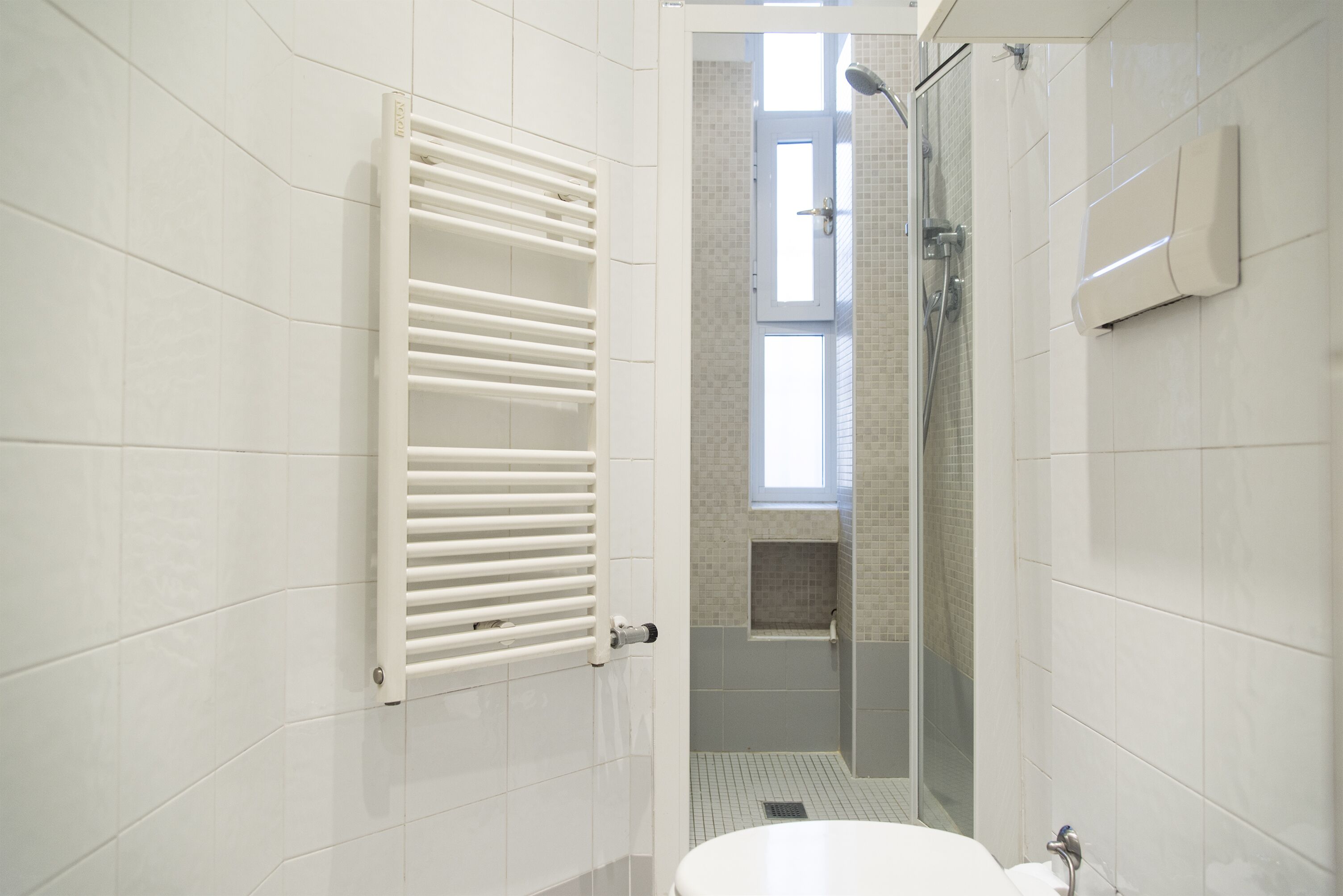 Une salle de bain moderne avec des carreaux blancs, des toilettes blanches, une douche à parois de verre et un porte-serviettes.