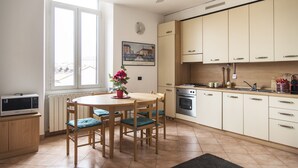 A kitchen with a dining table, chairs, a microwave, cabinets, and a window with a view. - Typical Apartment on River Naviglio / Darsena (Milan)