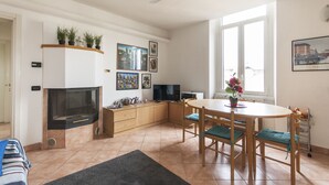 A modern living room with a fireplace, a dining table with chairs, a television, and a ceiling fan. - Typical Apartment on River Naviglio / Darsena (Milan)