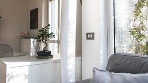 A modern living room with a grey sofa, a potted plant, and a large window providing natural light. - The Traveller's Terrace (Milan)