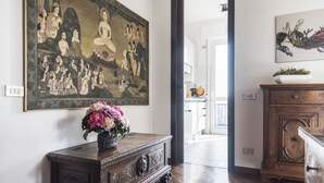 A hallway with a large Buddha painting, a wooden cabinet with a vase of flowers, and a wooden cabinet with a plant. - The Traveller's Terrace (Milan)