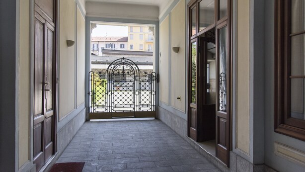 A corridor with a tiled floor, large wooden doors, and a metal gate at the end. - Bright & Cozy Flat near Navigli, Iulm, Tortona (Milan)