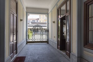 A corridor with a tiled floor, large wooden doors, and a metal gate at the end.
