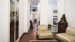 A hallway with arched doorways leading to a living area with two patterned sofas and a wooden cabinet.