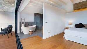 Un dormitorio moderno con una cama grande, un baño con bañera independiente y una zona con terraza de madera.