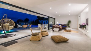 Una sala de estar moderna con un muro de cristal, muebles de mimbre y vistas al exterior.