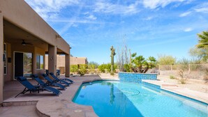 Una piscina con sillones de descanso y una zona cubierta, rodeada de vegetación desértica.