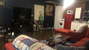 Een woonkamer met een rode bank, een televisie, een salontafel en een keukenhoek met een magnetron en fornuis.