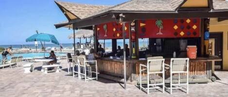 A beachside bar with outdoor seating and a pool in the background.