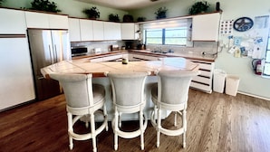Una cocina con una isla central, taburetes de bar, un refrigerador, microondas y varios electrodomésticos.