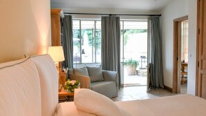 Une chambre d’hôtel avec un grand lit, un canapé, une table de chevet avec une lampe, et une vue sur l’extérieur grâce à de grandes fenêtres.