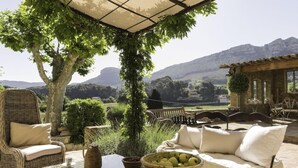 Une terrasse dotée de meubles en osier, une table sur laquelle se trouve un saladier rempli de fruits, et une vue sur les montagnes.
