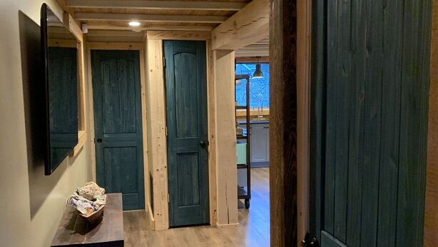 Un corridoio con pavimento in legno, porte, una panca e un televisore a parete.