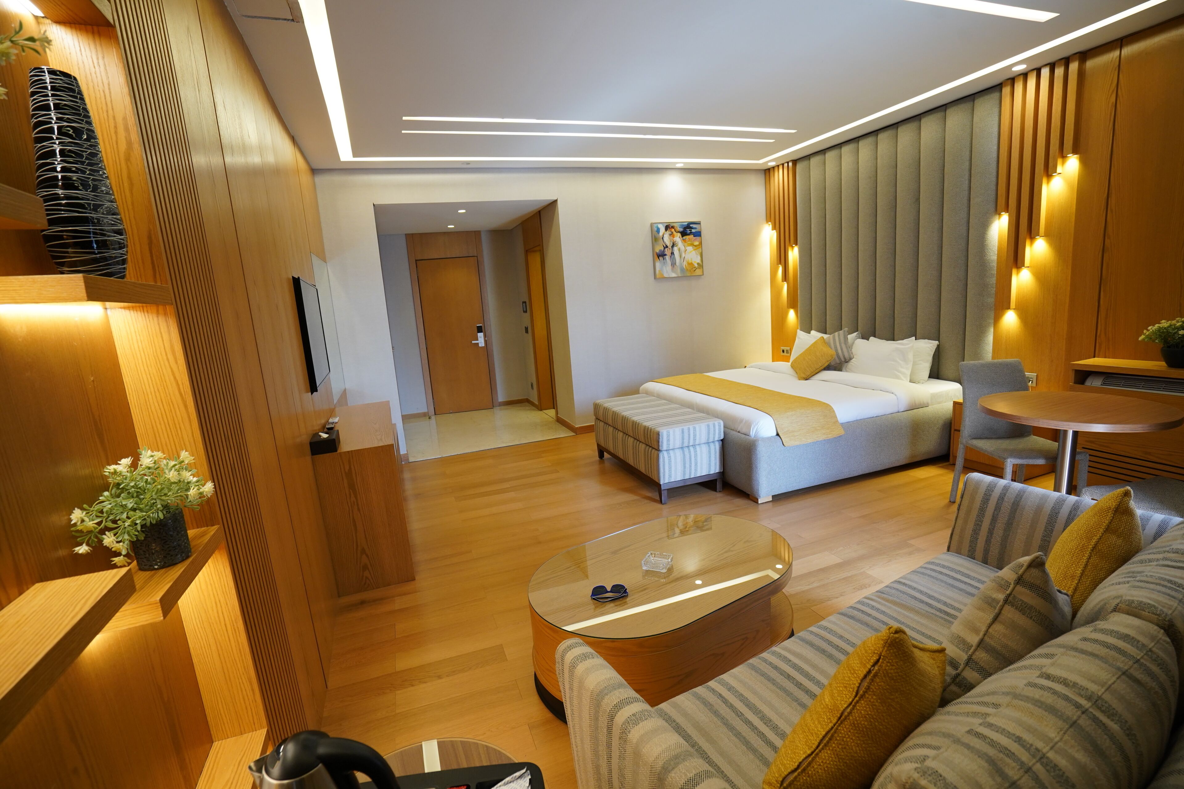 A modern hotel room with a large bed, a sofa, a coffee table, and a small table with a plant.